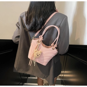 Detail view of pink shoulder bag with bear pendant and knotted handle on gray blazer