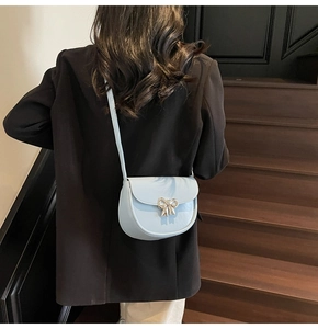 Light blue faux leather saddle bag with silver bow clasp worn on a wooden staircase