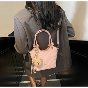 Detail of pink shoulder bag with wavy texture, bear charm, and striped silk scarf