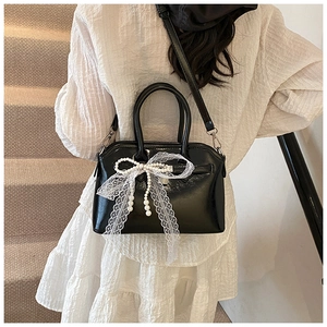 Detail of black glossy handbag with lace bow and pearl chain on white dress