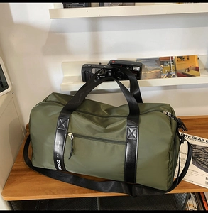 Sac de voyage vert olive avec logo NOCO sur les poignées noires, scène de style de vie