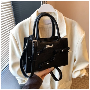 Close-up of black crossbody bag featuring bow accents, pearls, and detachable strap
