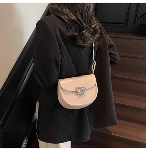 Close-up of light pink saddle bag with silver bow buckle on model in black suit