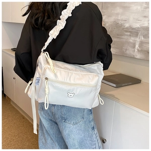 Detail of nylon crossbody bag with ruffled strap, knotted zippers and bear embroidery