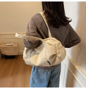Detail showing the side pocket and logo tag on a beige canvas cylindrical shoulder bag
