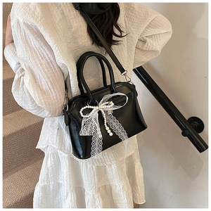 Detail of black glossy leather bag with white lace bow and pearl pendant decoration