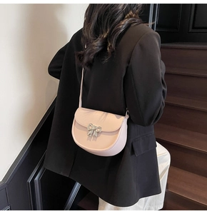 Model wearing peach pink saddle bag with silver bow buckle on black suit background