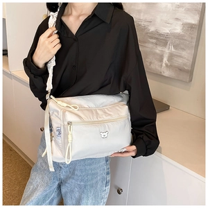 Detail of nylon crossbody bag featuring a pleated shoulder strap and cute bear badge