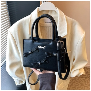 Close-up of black crossbody bag with three pearl-studded bows and a metallic logo