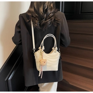 Detail of white wave-textured crossbody bag with twisted handles and plush bear charm