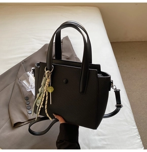 Détail du sac seau noir texturé avec cordon rayé et pendentif boule jaune élégant