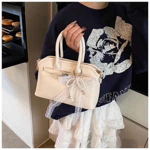 Close-up of cream square handbag featuring lace bow and elegant pearl charm detail
