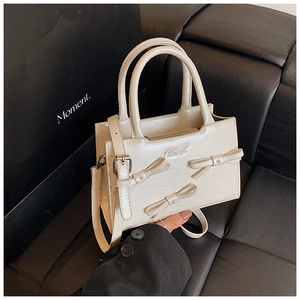 Detail of a beige bow-knot crossbody bag held by a model on a leather sofa