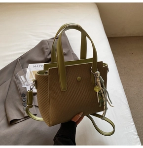 Détail du sac seau tissé vert olive avec poignée épaisse et breloque tressée élégante
