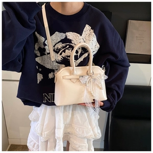 Detail of off-white crossbody bag featuring lace mesh and pearl bow charm accessory