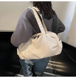 Detail of a large beige canvas travel bag with wide straps shown on a person