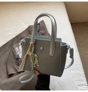 Détail du sac seau tissé gris avec anses en cuir bleu et breloque ours blanc mignon