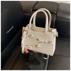 Detailed close-up of cream bow handbag with pearl accents and versatile carry straps