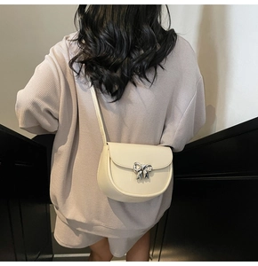 Detail of cream saddle bag featuring a silver bow buckle on glossy leather material