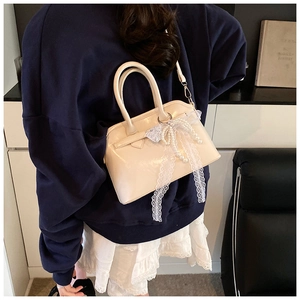 Detail of creamy white crossbody bag with elegant lace bow and decorative pearls