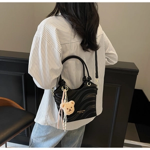 Detail of black wavy textured shoulder bag with golden hardware and teddy bear charm