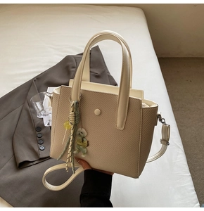 Détail du sac seau beige avec texture tissée, breloque chien et ruban rayé chic