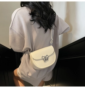 Detail of cream saddle bag with silver bow ornament worn as a crossbody style