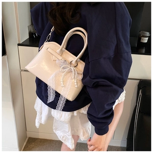 Detail of creamy white leather crossbody bag with lace bow and pearl tassel accents