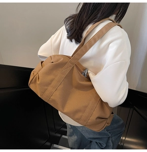 Brown canvas travel bag with zip closure shown in use on a model's shoulder