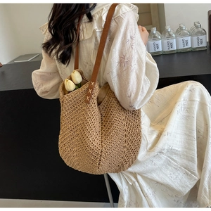 Detail of woven straw tote bag with brown leather straps shown on a model's shoulder