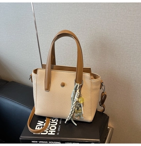 Détail du sac seau tissé beige avec poignées en cuir marron et pendentif ours