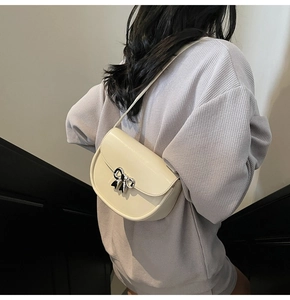 Detail view of a cream white saddle bag with a silver butterfly metal clasp on a model