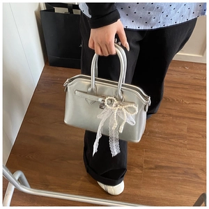 Close-up of silver handbag featuring pearl bow decoration and white lace charm