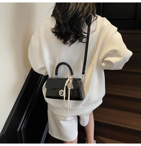Vue arrière d'un mannequin portant un sac en cuir verni noir avec foulard et breloque cloche