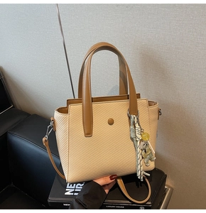 Détail du sac seau tressé avec bordure en cuir et breloque décorative en forme d'ours