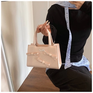 Detailed view of light pink leather handbag featuring three pearl-embellished bows and top handles