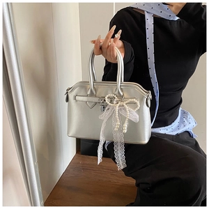 Silver metallic handbag featuring a decorative metal lock and a lace pearl bow charm
