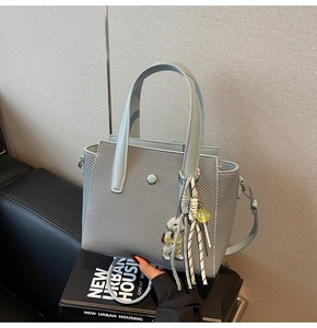 Détail du sac seau tissé bleu-gris clair avec breloque ours et bandoulière amovible