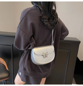 Silver saddle bag featuring a metallic finish and elegant bow buckle on a model