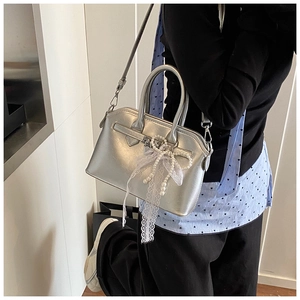 Detailed view of silver trapezoid handbag with lace bow and pearl chain charm accessory