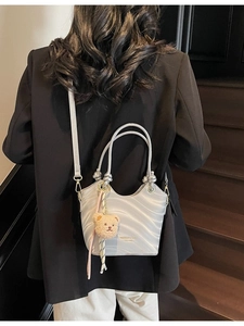 Silver shoulder bag with wave texture and plush bear charm shown on a model