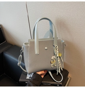 Détail d'un sac seau tissé bleu clair avec pendentif ours sur surface texturée