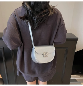 Detail of silver saddle bag with metal bow buckle worn by a model on a crossbody strap