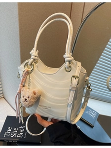 Chic beige textured shoulder bag with wavy pattern, plush bear charm, and top handle