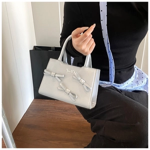 Detail of grey crossbody bag with decorative bows and stylish metallic finish