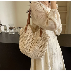 Detail of the woven beach tote showing brown leather straps and X-shaped stitching details