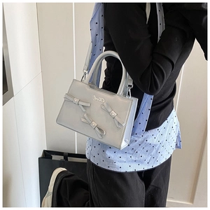 Detail of glossy silver handbag with decorative bows and detachable shoulder strap