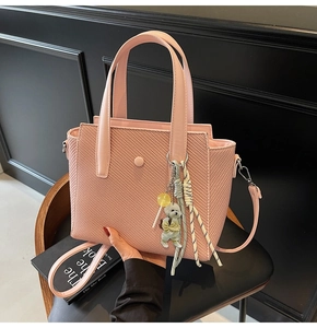 Détail du sac seau rose tissé avec breloque ours et bandoulière sur fond noir élégant