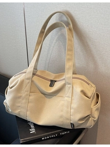 Beige canvas travel duffel bag with large capacity and crossbody strap on black magazines