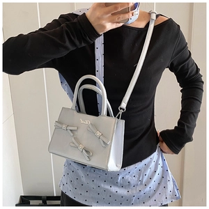 Detail of light blue bow handbag with silver metal logo and crossbody strap
